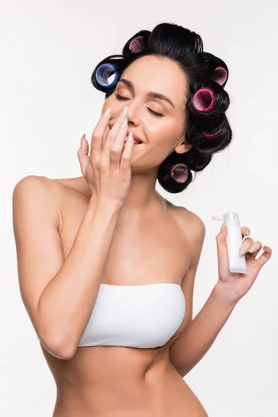 Mujer joven con los ojos cerrados en los rulos y la parte superior de la aplicación de crema en la nariz y la celebración de tubo aislado en blanco - foto de stock