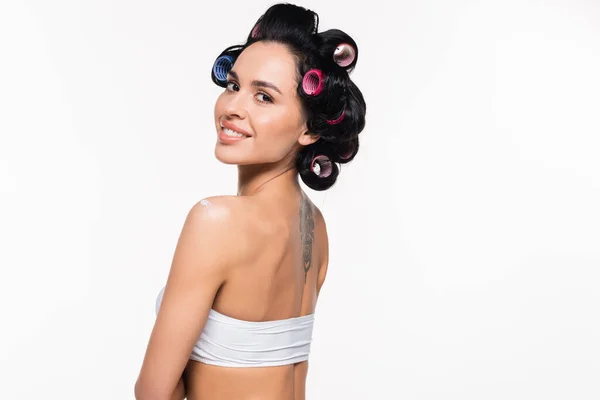 Sorrindo jovem mulher em rolos e tatuagem nas costas posando com creme aplicado no ombro isolado no branco — Fotografia de Stock