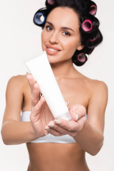 Cream tube in hands of blurred smiling young woman in curlers isolated on white — Stock Photo