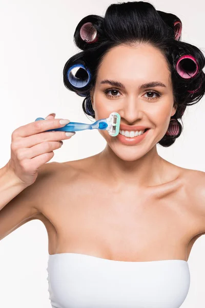 Positive young woman in curlers holding razor near face isolated on white — Stock Photo