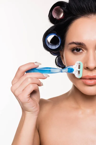 Portrait of serious young woman in curlers holding razor near face isolated on white — Stock Photo