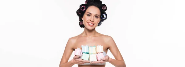 Allegra giovane donna in bigodini che tiene piccole scatole regalo in mani isolate su bianco, striscione — Stock Photo