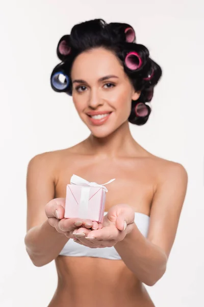 Smiling young woman in curlers holding small gift box in hands isolated on white — Stock Photo