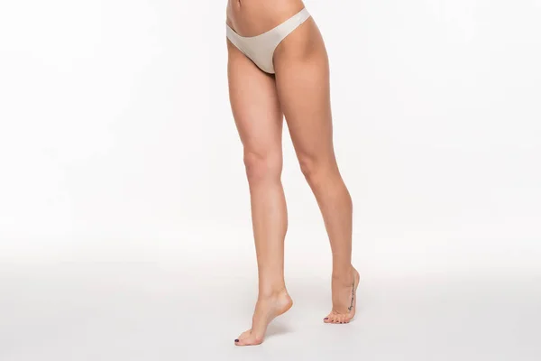 Partial view of young woman in beige panties and with fit legs standing on tiptoes on white — Stock Photo