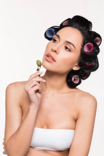 Young woman in curlers making facial massage with jade roller isolated on white — Stock Photo