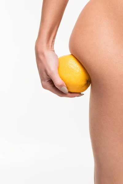 Vista de cerca de la mujer joven haciendo masaje anti-celulitis de nalga con naranja aislado en blanco - foto de stock