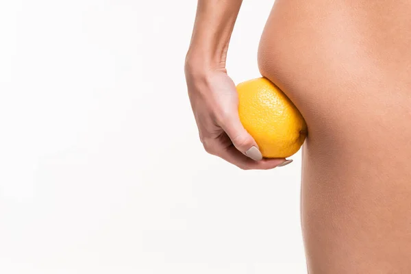 Vista de cerca de la mujer joven haciendo masaje anti-celulitis de nalga con naranja en la mano aislado en blanco - foto de stock