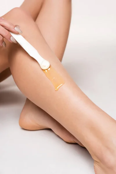 Vue partielle de la jeune femme appliquant de la cire d'épilation sur la jambe avec une peau lisse sur le blanc — Photo de stock