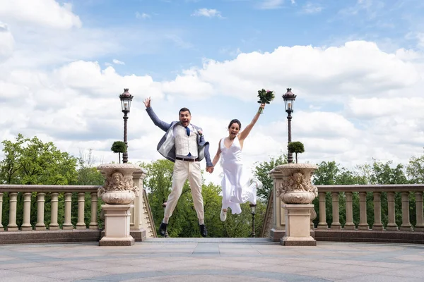 Happy newlyweds with bouquet jumping in park — Stock Photo
