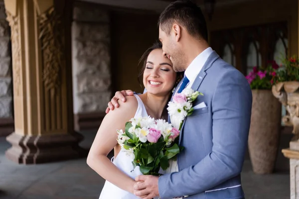 Жених обнимает счастливую невесту с букетом на открытом воздухе — стоковое фото