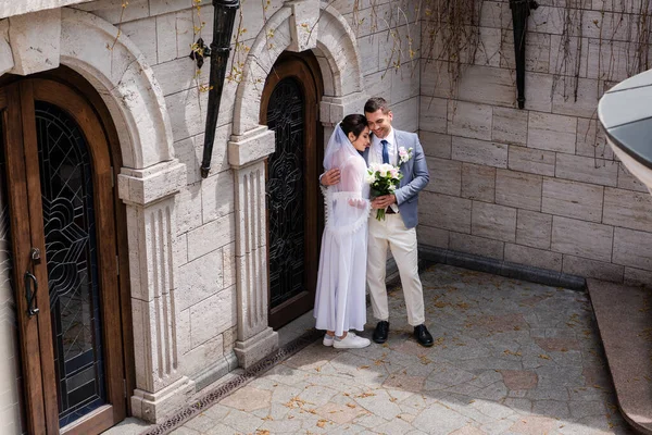 Sonrientes recién casados abrazándose cerca del edificio al aire libre - foto de stock