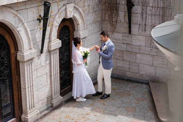 Vista lateral do noivo segurando a mão da noiva com buquê perto do edifício — Fotografia de Stock