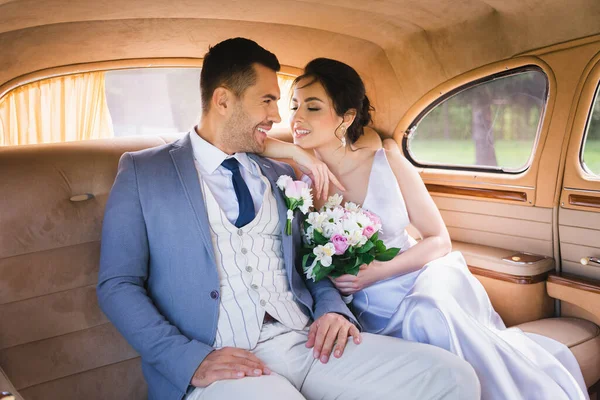 Sposa sorridente guardando lo sposo in auto retrò — Foto stock