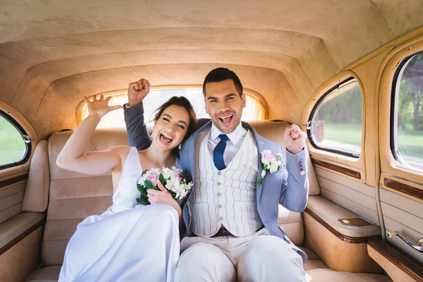 Excited newlyweds showing yes gesture in vintage car — Stock Photo