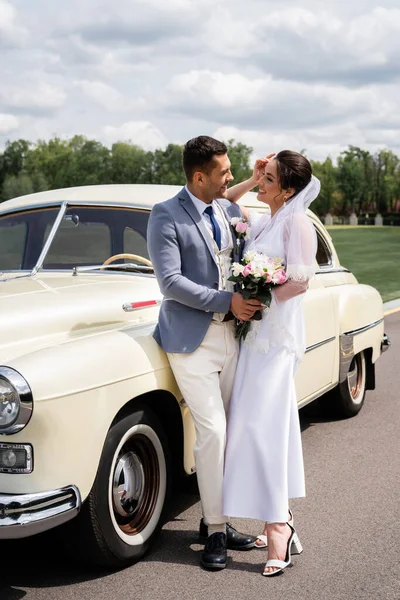 Side view of smiling newlyweds standing near vintage car — Stock Photo