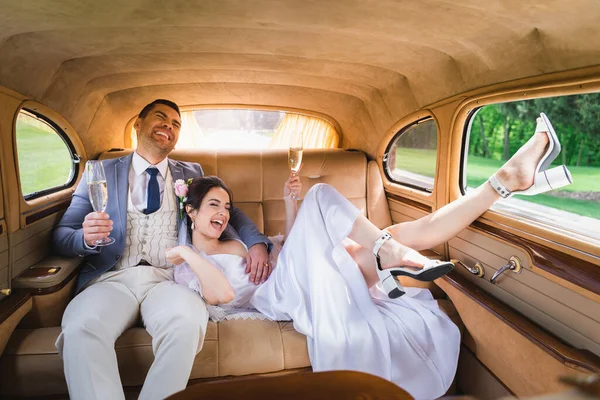 Щаслива наречена тримає келих шампанського біля нареченого в ретро-авто — стокове фото