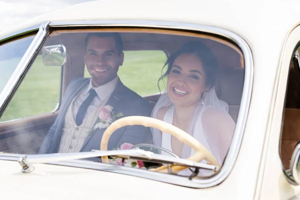 Усміхнена наречена і наречений дивиться на камеру з ретро-автомобіля — стокове фото
