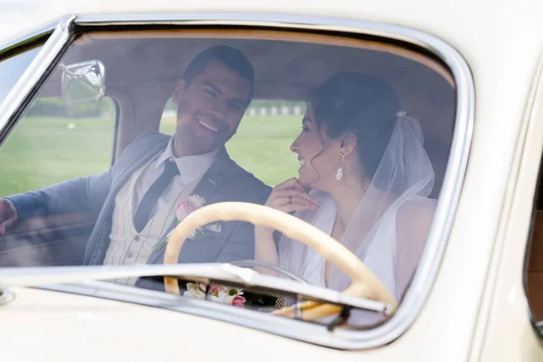 Cheerful bride and groom looking at each other in retro car — Stock Photo