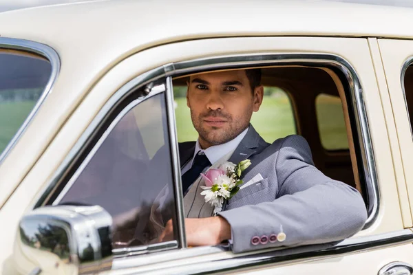 Elegant groom looking at camera in vintage car — Stock Photo