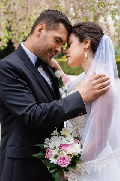 Vista lateral de jovens recém-casados abraçando com os olhos fechados no parque — Fotografia de Stock