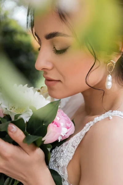 Vista lateral de la novia joven sosteniendo ramo en primer plano borroso - foto de stock