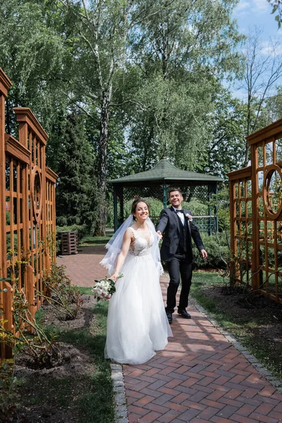 Happy bride and groom walking on walkway in park — Stock Photo