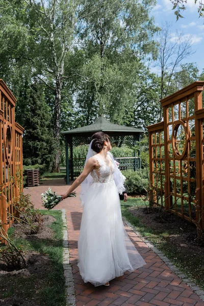 Молодая невеста с букетом прогулка возле жениха в парке — стоковое фото
