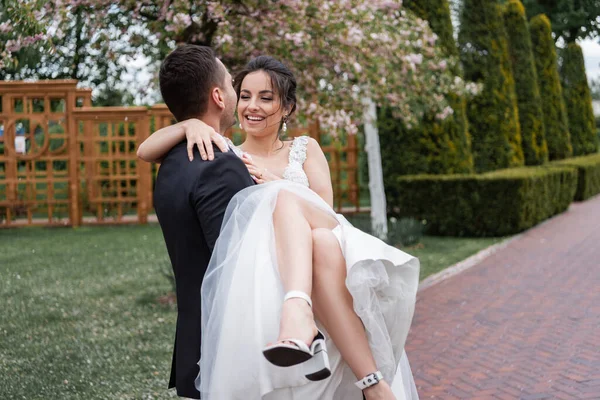 Noivo segurando as mãos sorridente noiva no vestido de casamento branco no parque — Fotografia de Stock
