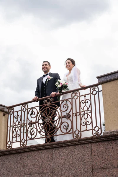 Visão de baixo ângulo de recém-casados sorridentes em pé na ponte — Fotografia de Stock