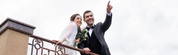 Niedrige Ansicht des Bräutigams, der mit dem Finger in der Nähe von Braut und Geländer im Freien zeigt, Banner — Stockfoto