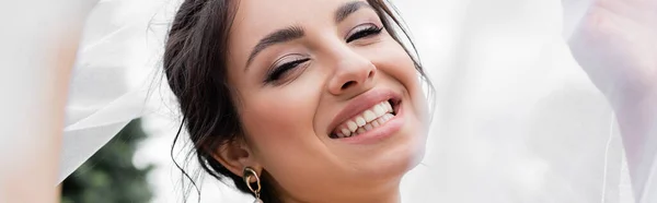 Novia alegre sosteniendo velo blanco al aire libre, bandera - foto de stock