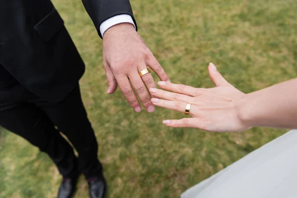 Vista recortada de anillos de oro en manos de recién casados al aire libre - foto de stock