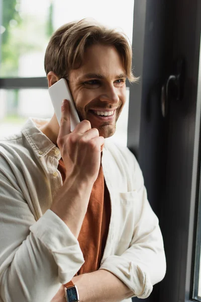 Jovem sorridente em camisa bege falando no celular no escritório moderno — Fotografia de Stock
