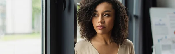 Portrait of thoughtful african american woman standing near window in modern office, banner — Stock Photo