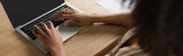 Teilansicht einer jungen afrikanisch-amerikanischen Frau, die am Schreibtisch sitzt und im modernen Büro auf dem Laptop tippt, Banner — Stockfoto