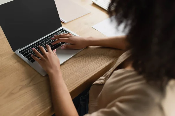 Visão parcial da jovem afro-americana sentada à mesa e digitando no laptop no escritório moderno — Fotografia de Stock