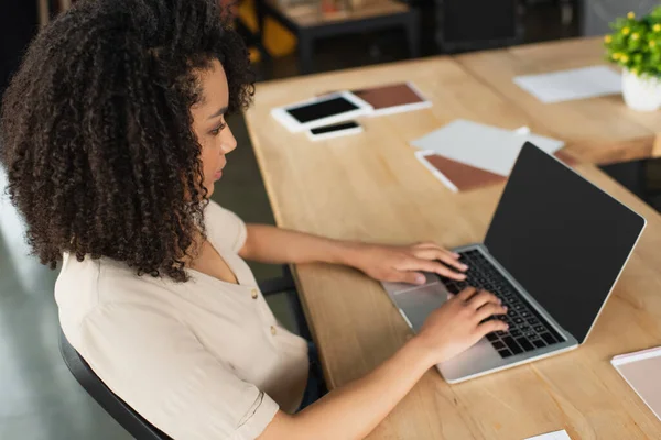 Visão de alto ângulo da jovem mulher afro-americana séria digitando no laptop no escritório moderno — Fotografia de Stock