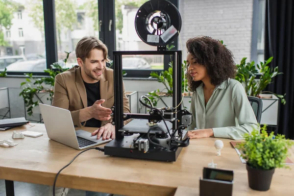 Jeunes collègues interracial travaillant avec imprimante 3D et ordinateur portable dans un bureau moderne — Photo de stock