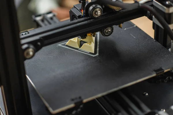 Close up view of 3D printer creating plastic model near blurred figures and laptop in office — Stock Photo