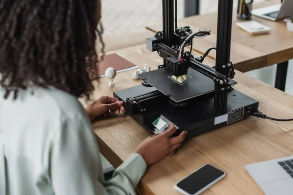 Young designer working with 3D printer near produced plastic models on table in modern office — Stock Photo