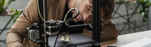 Focused young designer looking at 3D printer producing model in modern office, banner — Stock Photo