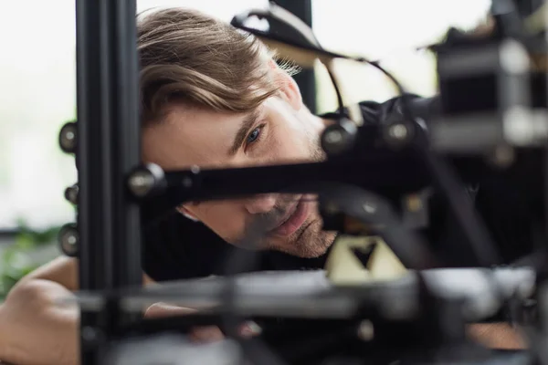 Vista de cerca del joven diseñador mirando a la impresora 3D de trabajo en la oficina - foto de stock