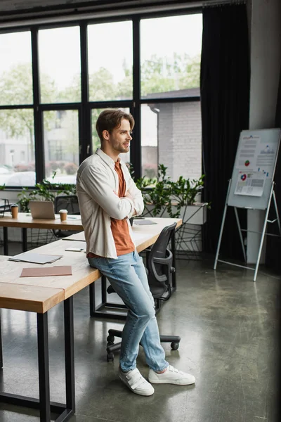 Thoughtful young man in casual clothes with crossed arms standing in modern open space — Stock Photo