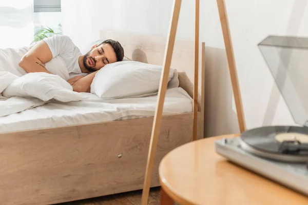 Young man sleeping near vinyl player on blurred foreground — Stock Photo