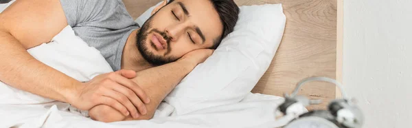 Blurred alarm clock near sleeping man at home, banner — Stock Photo