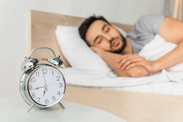 Réveil sur la table près d'un homme flou dormant sur le lit — Photo de stock