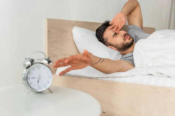 Man waking up near blurred alarm clock in bedroom — Stock Photo