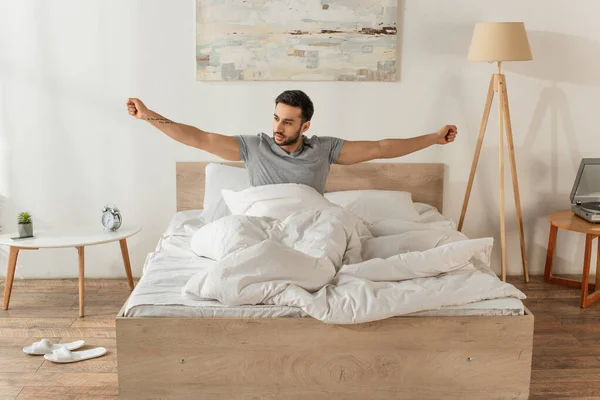 Bearded man stretching while sitting on bed in morning — Stock Photo