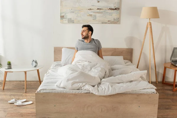 Вид сбоку на человека, сидящего дома на кровати — стоковое фото