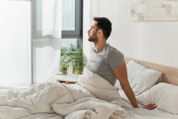 Side view of young bearded man sitting on bed — Stock Photo